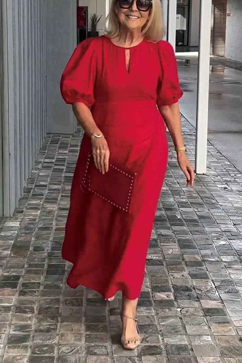 Woman in red puff sleeve dress, holding clutch, walking on tiled path with modern gray wall backdrop.