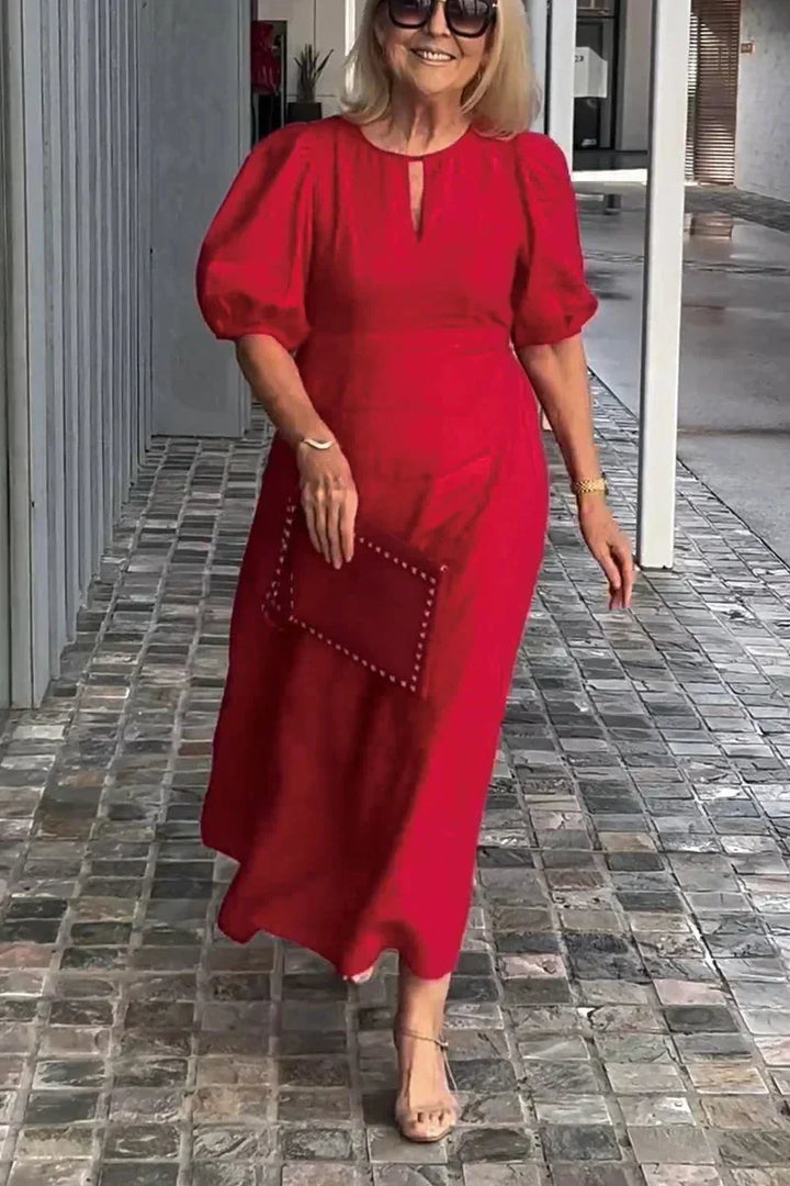 Woman in red puff sleeve dress, holding clutch, walking on tiled path with modern gray wall backdrop.