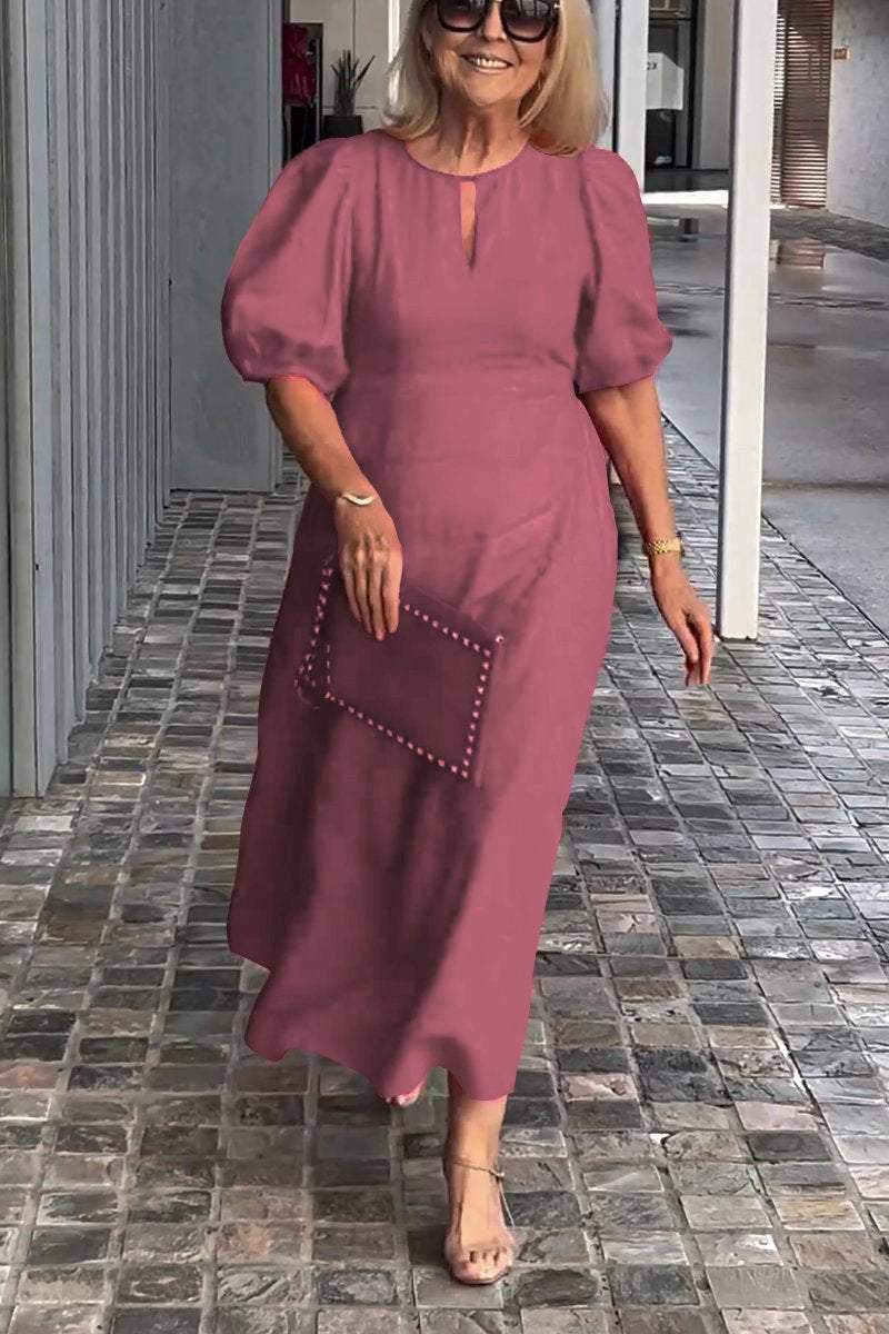 Woman in pink puff sleeve dress, holding clutch, walking on tiled path with modern gray wall backdrop.