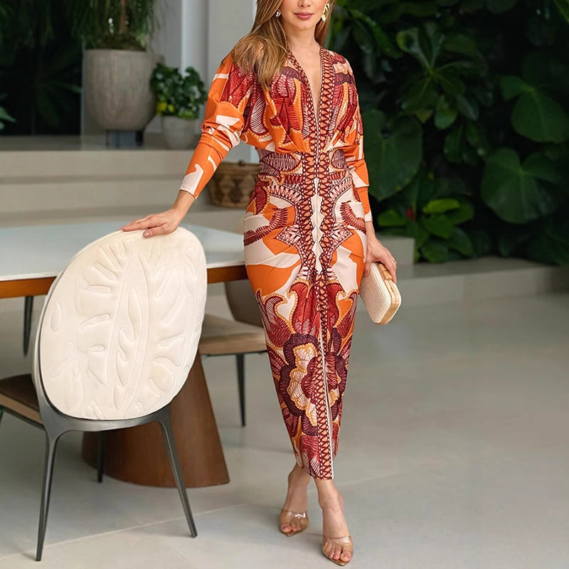 Elegant V-neck dress with vibrant orange and red patterns, modeled indoors beside a modern dining set.
