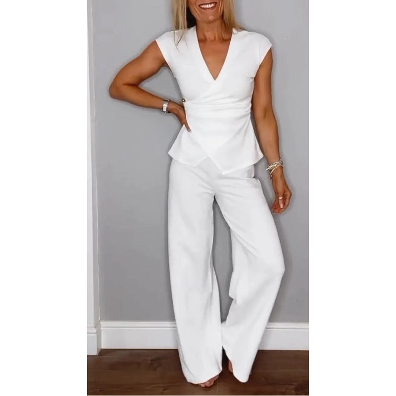 Elegant white top with V-neck and flared pants, worn by a smiling woman in a studio setting against a gray wall.
