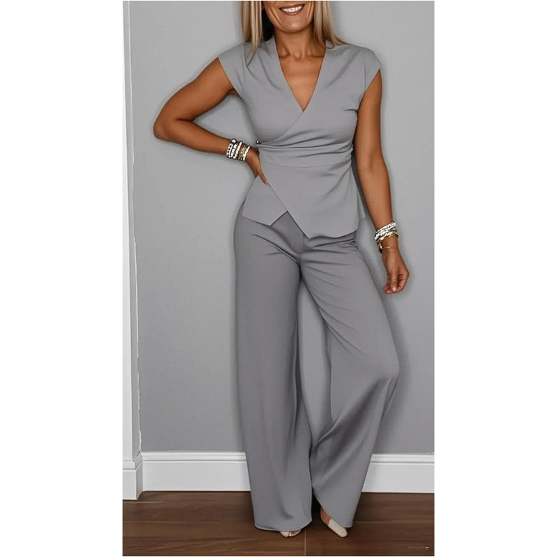 Stylish light gray V-neck top and flared pants, worn by a smiling woman in a gray-walled indoor studio.