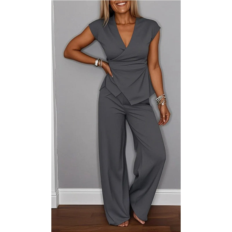 Elegant dark gray V-neck top and flared pants, modeled by a smiling woman in a studio with a gray background.