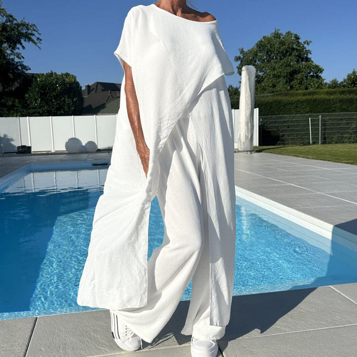 Elegant white off-shoulder two-piece set with flowing pants by a pool, featuring a relaxed, breezy design on a sunny day.