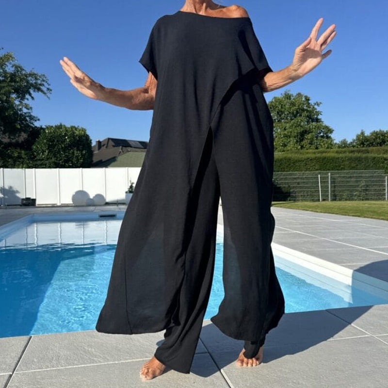 Chic black off-shoulder two-piece ensemble with wide-leg pants, modeled poolside in a serene outdoor setting.