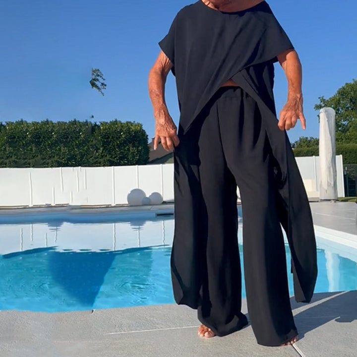 Stylish black two-piece outfit with off-shoulder top and flowing pants, set against a backdrop of a pool and greenery.