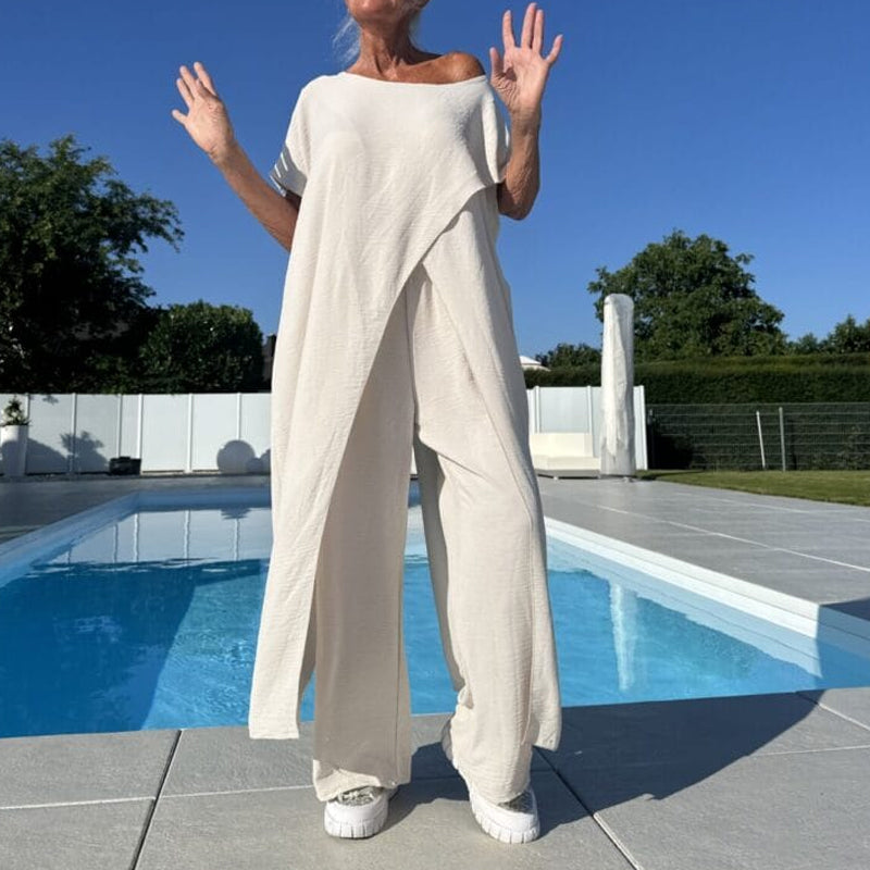 Cream off-shoulder two-piece set with flowing style, shown with arms raised, next to a pool on a sunny day.