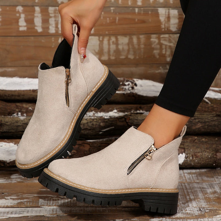 Cream ankle boots with zipper detail, held in hand against a wooden background.