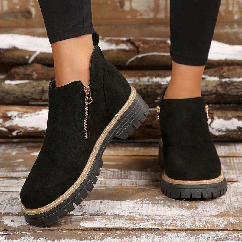 Black ankle boots with zipper, worn with leggings on a rustic wooden background.