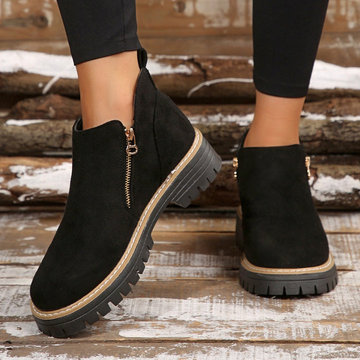 Black ankle boots with zipper, worn with leggings on a rustic wooden background.