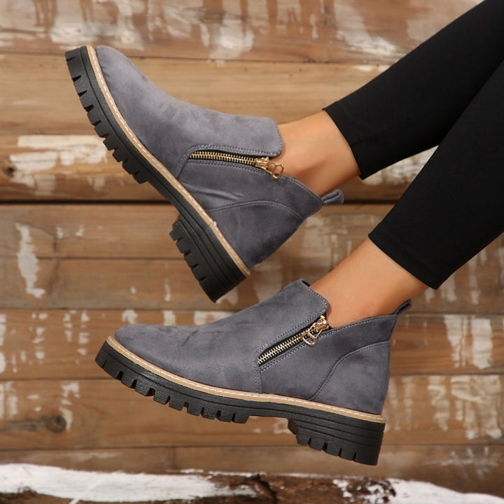 Gray ankle boots with zipper, worn with leggings against a rustic wooden wall.
