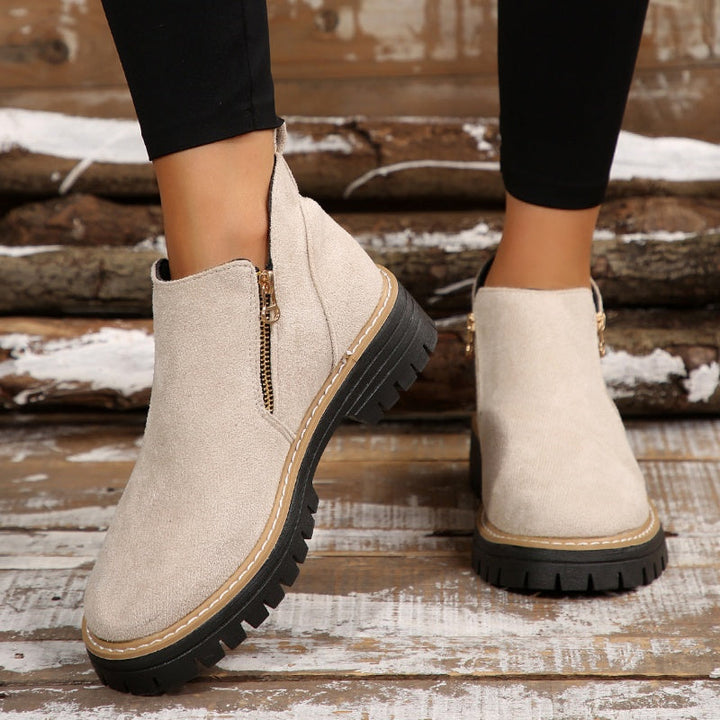 Cream ankle boots with zipper, worn with leggings on rustic wooden floor.