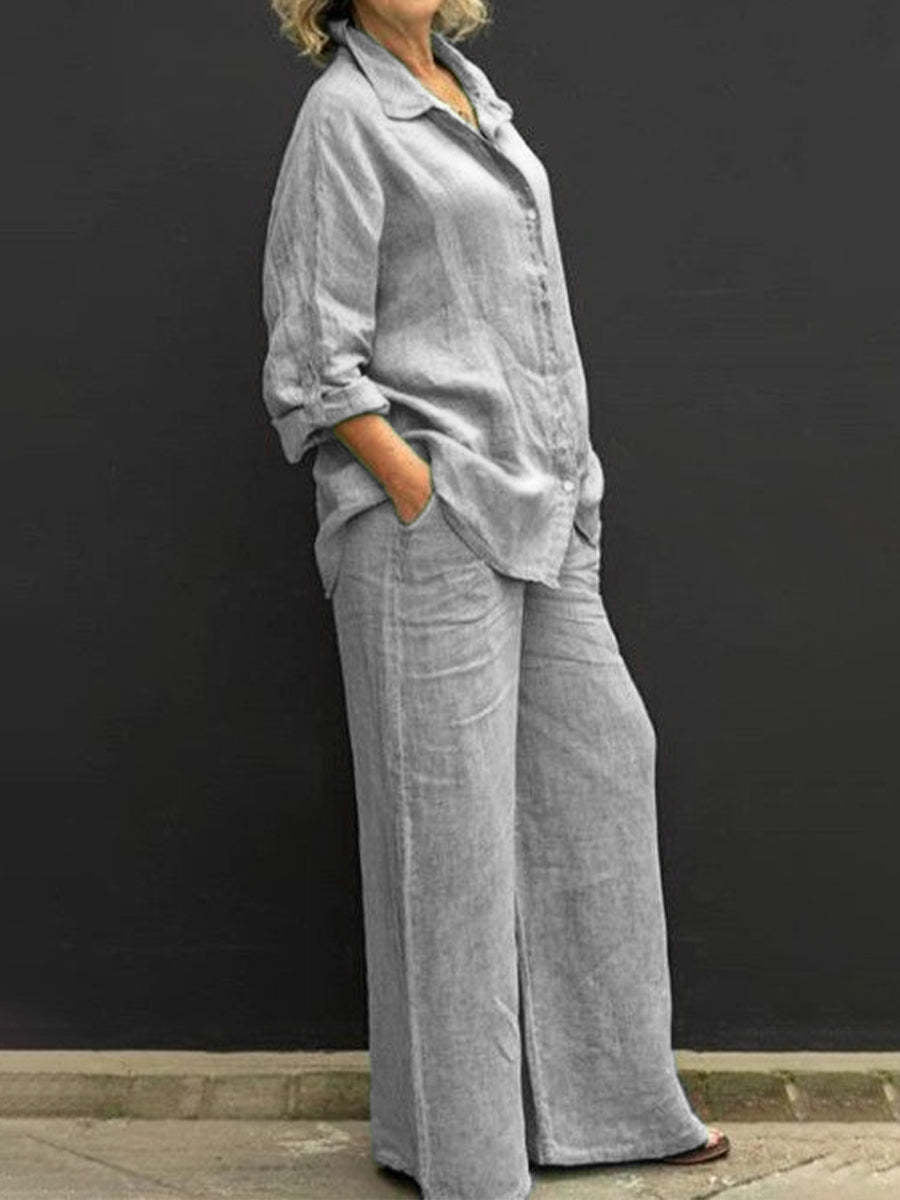 Gray effortless elegant set with long sleeves and wide-leg pants, worn by a woman against a black wall.