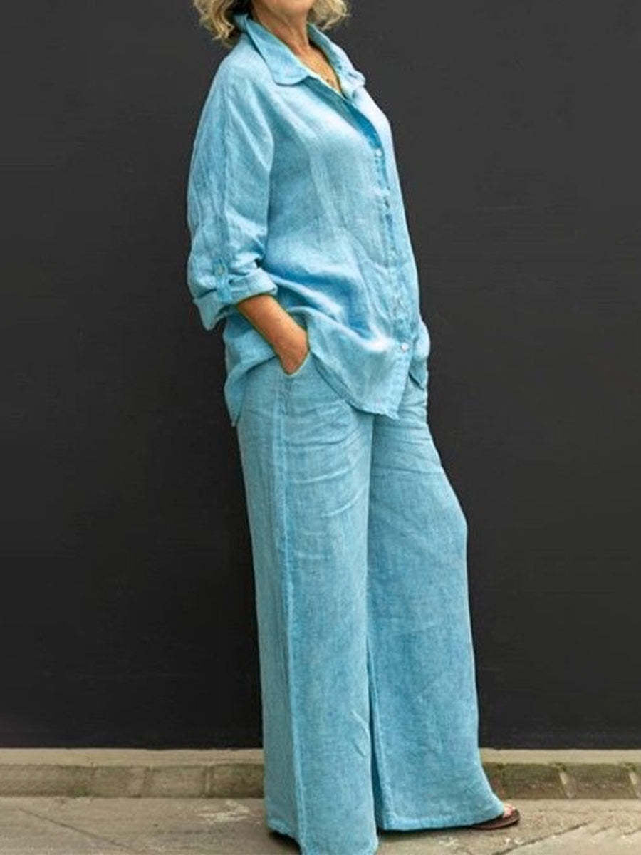 Blue effortless elegant set with long sleeves and wide-leg pants, worn by a woman against a black wall.