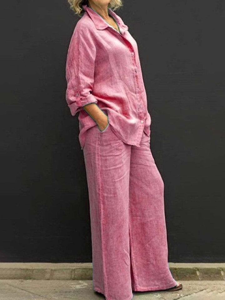 Pink effortless elegant set with long sleeves and wide-leg pants, worn by a woman against a black wall.