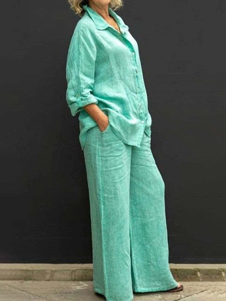 Teal effortless elegant set with long sleeves and wide-leg pants, worn by a woman against a black wall.
