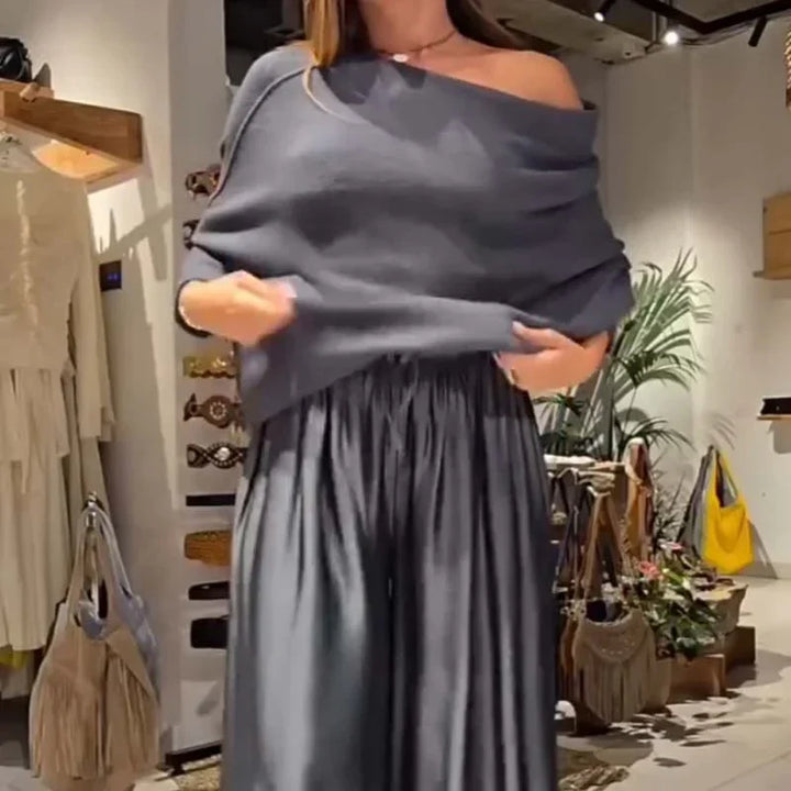 Model in a gray off-shoulder top and pants, adjusting the garment in a retail store.