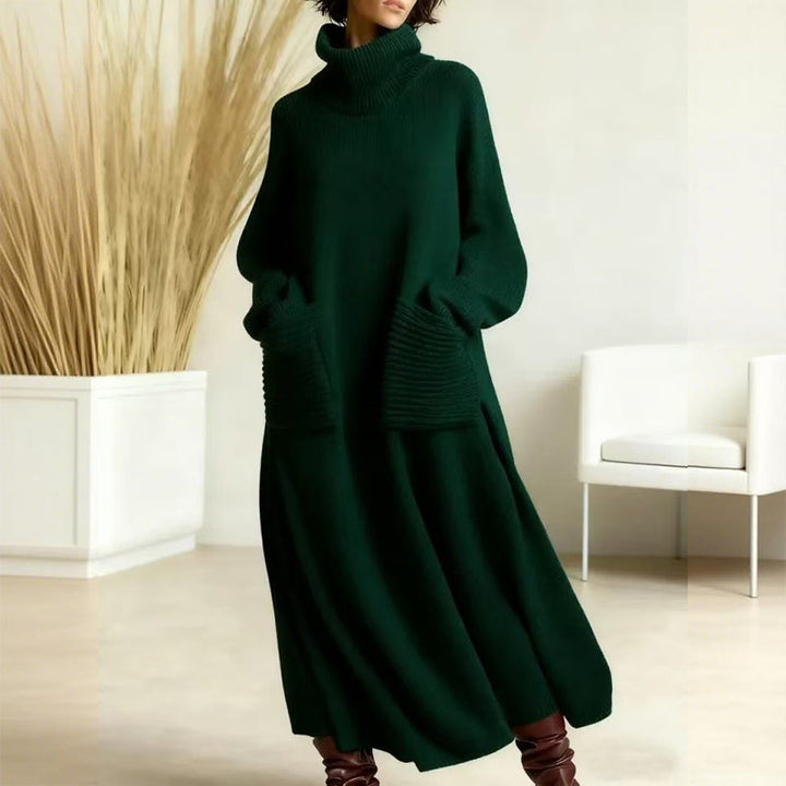 Chic dark green sweater dress with a high neck and prominent pockets, set in a neutral indoor environment with a clean background and white chair.