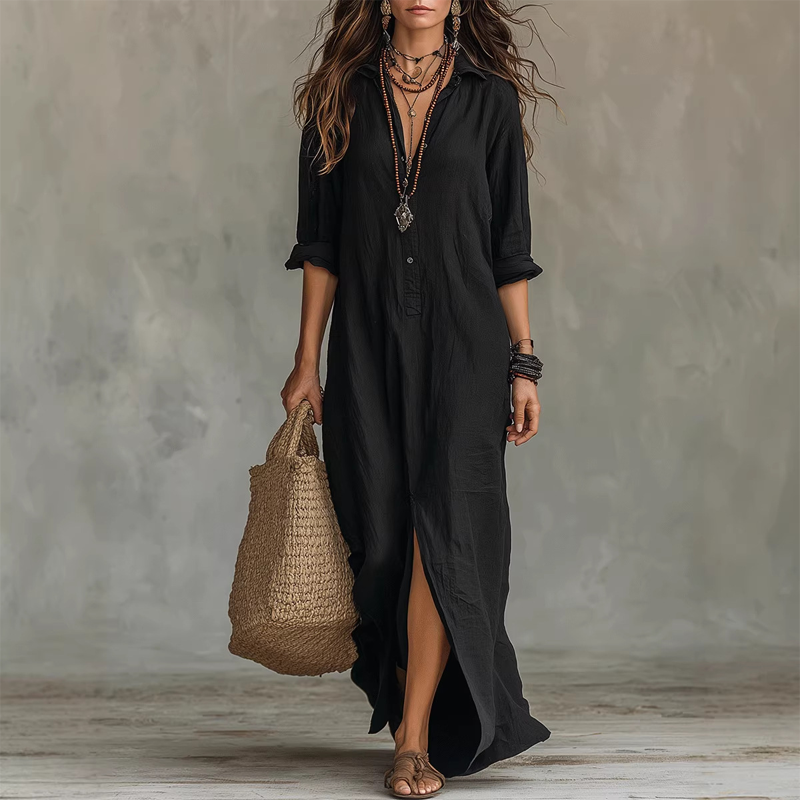 Black relaxed midi dress with button front, long sleeves rolled up, accessorized with layered necklaces, straw tote, against a neutral studio background.