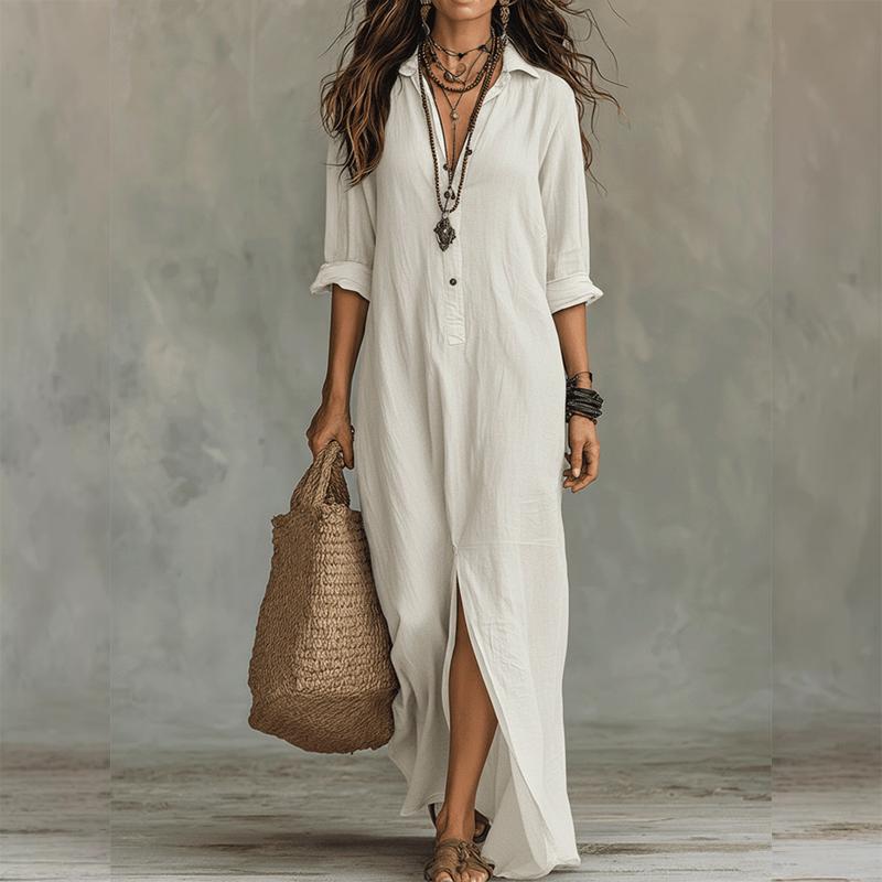 White relaxed midi dress with button front, long sleeves rolled up, styled with layered necklaces, straw tote, against a neutral studio background.