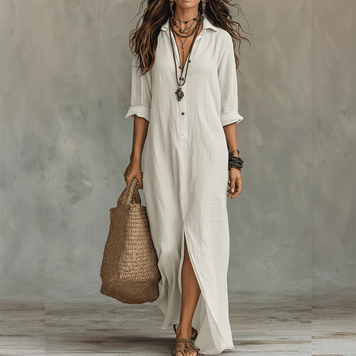 White relaxed midi dress with button front, long sleeves rolled up, styled with layered necklaces, straw tote, against a neutral studio background.