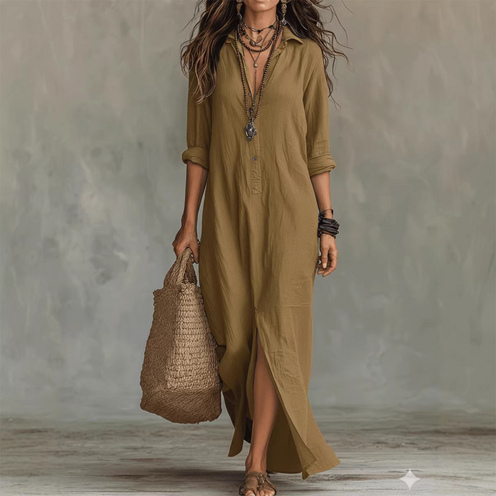 Beige relaxed midi dress with button front, long sleeves rolled up, styled with layered necklaces, straw tote, against a neutral studio background.