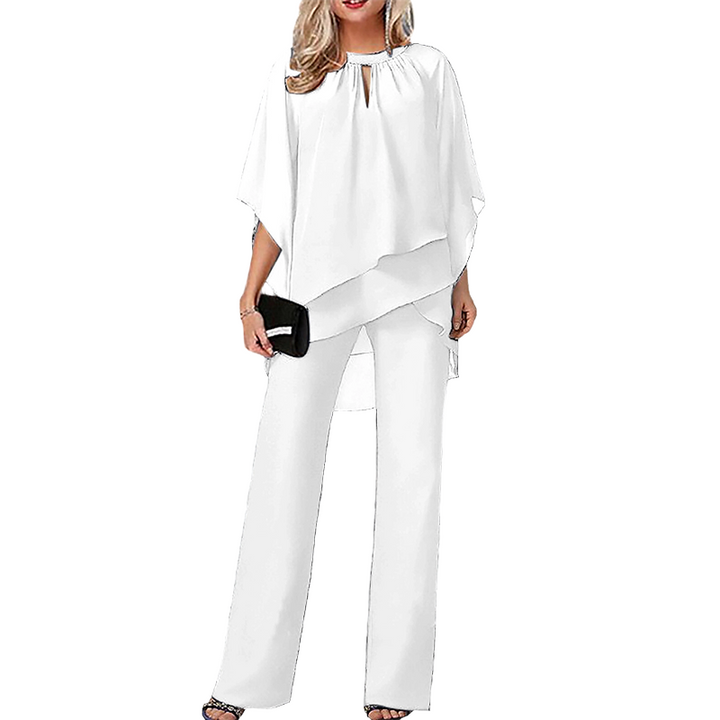 White elegant set, layered top and wide-leg pants, holding black clutch in studio.