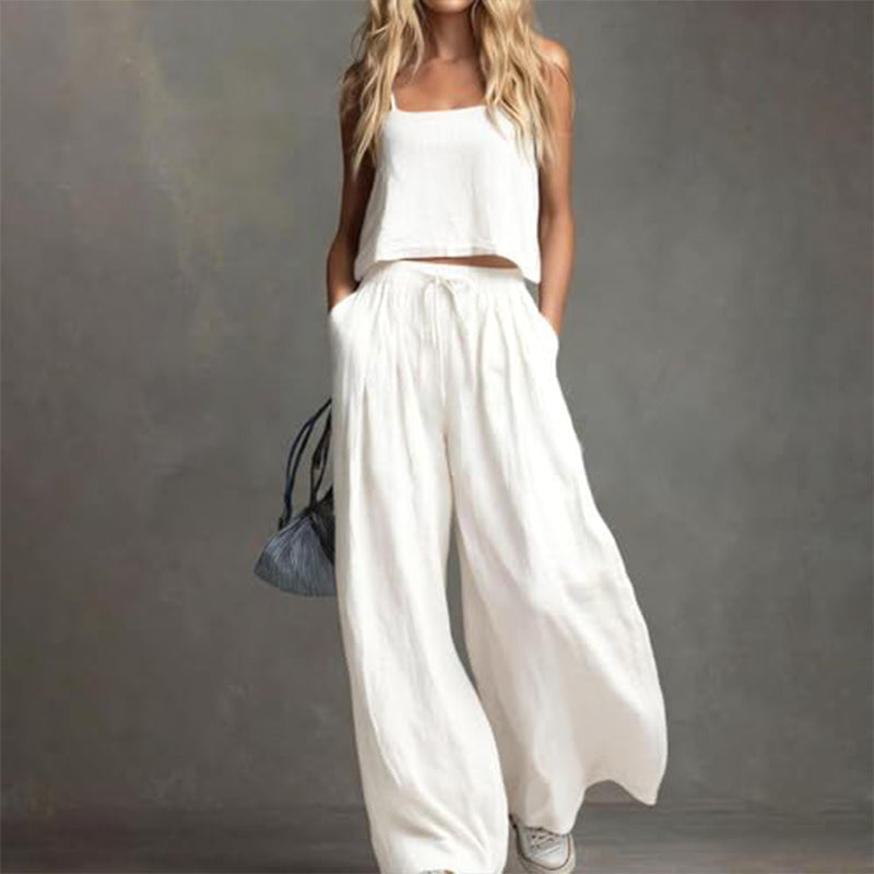 Woman in a stylish white set with a relaxed top and flowing wide-leg pants, carrying a bag. Studio background.