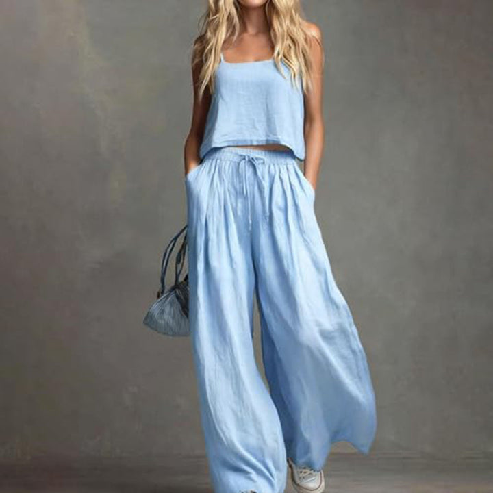 Woman modeling a light blue set with a relaxed top and spacious wide-leg pants, holding a bag. Studio backdrop.