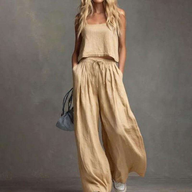 Woman dressed in a chic beige set featuring a loose top and wide-leg pants, with a small handbag. Studio setting.