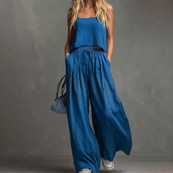 Woman showcasing a fashionable deep blue set with a flowing top and wide-leg pants, carrying a purse. Studio background.