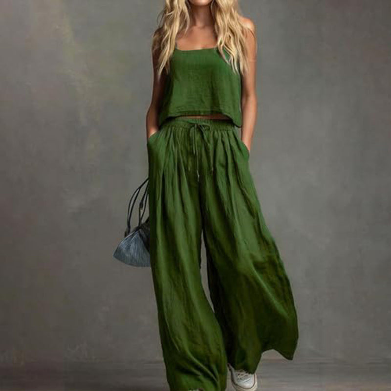 Woman displaying an elegant green set with a loose-fitting top and wide-leg pants, with a bag. Studio setting.