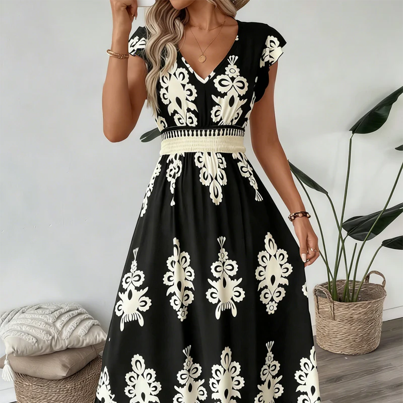 Black elegant long dress with white floral patterns and a smocked waist, worn indoors with plants and cushions.