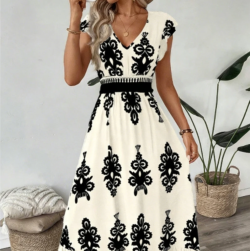 White elegant long dress with black floral patterns and a smocked waist, worn indoors with plants and cushions.