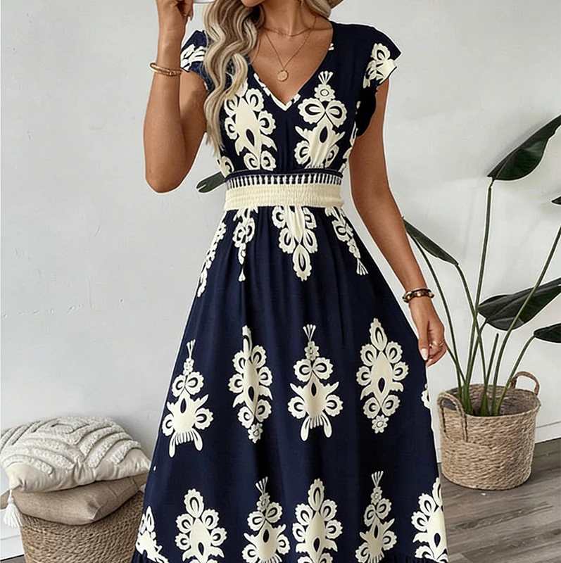 Navy blue elegant long dress with white floral patterns and a smocked waist, worn indoors with plants and cushions.