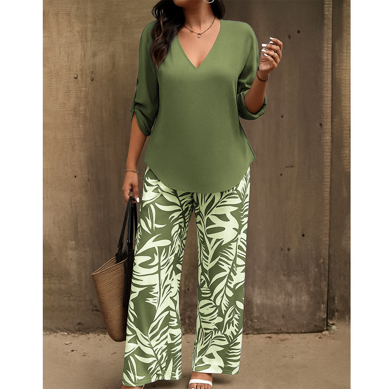Woman in olive green V-neck top and green leaf-print pants with a straw handbag in an outdoor setting.