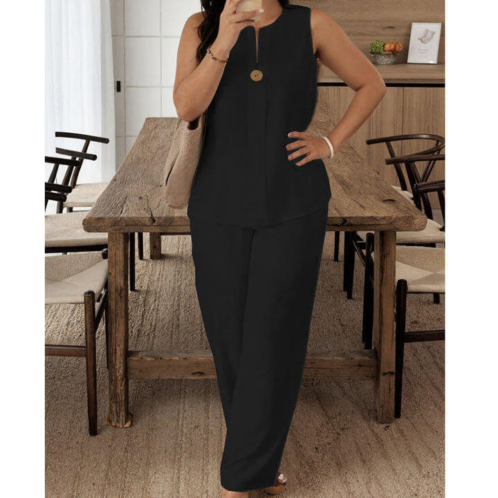 Elegant black sleeveless top and pants set modeled in a cozy dining room with rustic wooden chairs and a beige textured rug.