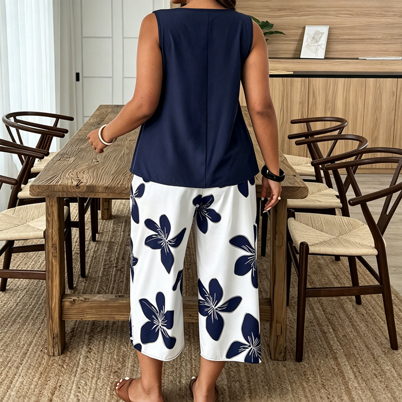 Back view of a woman in navy tunic and white floral pants standing in a dining room with wood furniture.