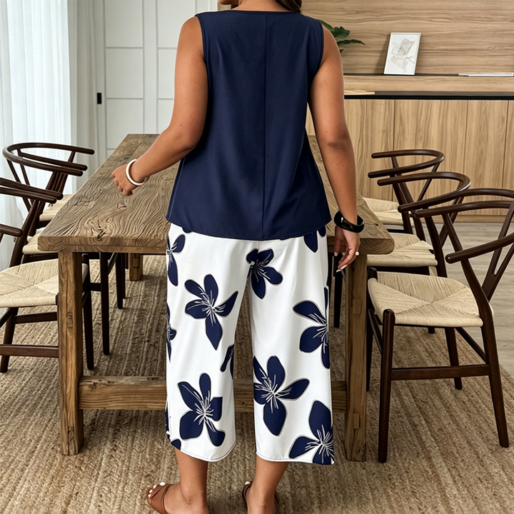 Back view of a woman in navy tunic and white floral pants standing in a dining room with wood furniture.