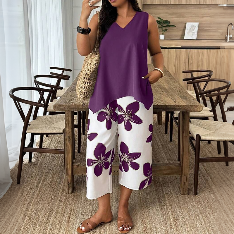 Woman in a violet tunic and white floral pants with a woven bag in a dining room with wooden furniture.