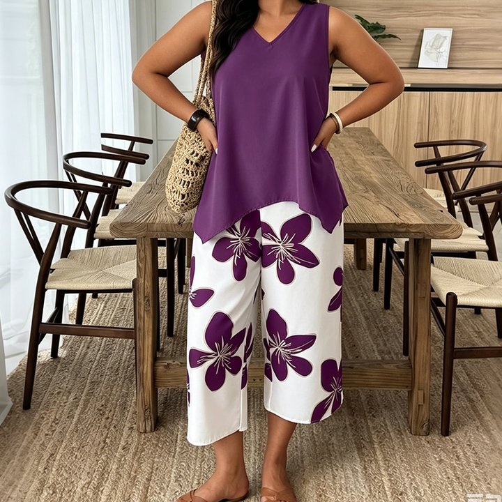 Woman posing in a violet tunic and white floral pants in a stylish dining room with wooden furniture.