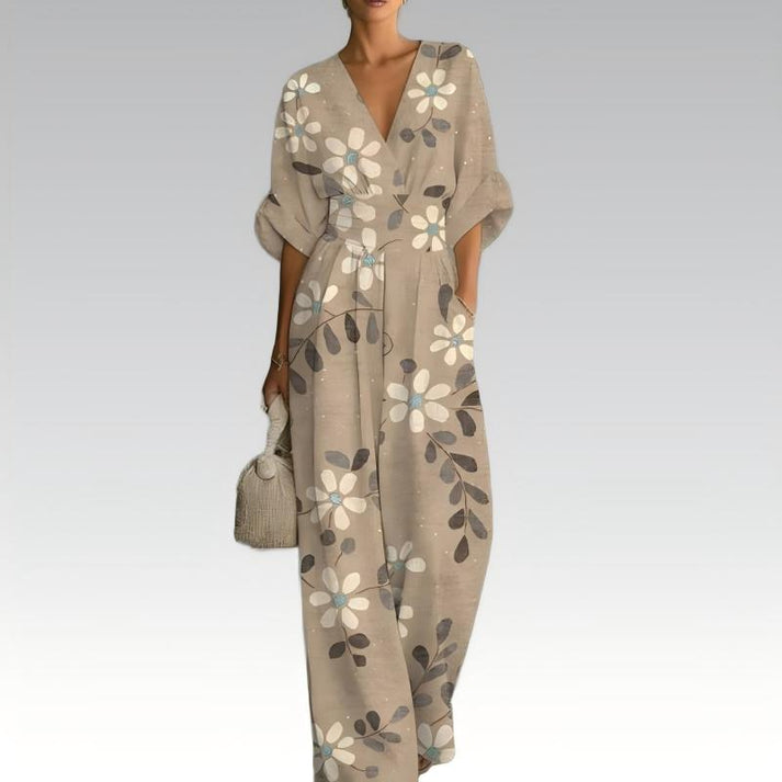 Taupe jumpsuit featuring large floral patterns, V-neckline, loose sleeves, paired with a woven handbag against a neutral background.