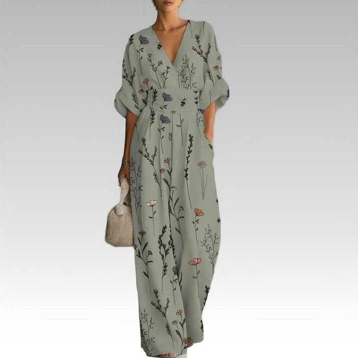Elegant jumpsuit with floral print in muted tones, deep V-neck, relaxed fit, carrying a woven handbag, on a neutral gradient background.