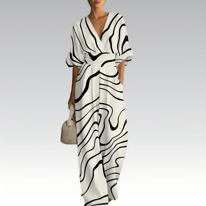 Black and white jumpsuit with bold, wavy lines, deep V-neck, fluid silhouette, accessorized with a woven handbag, on a neutral background.