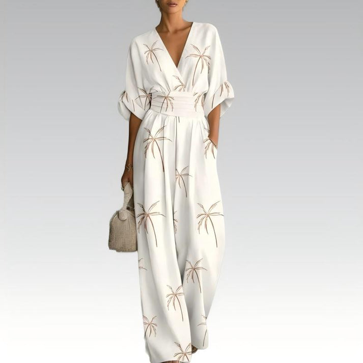 White jumpsuit adorned with palm motifs, elegant V-neck, gathered waist, styled with a handbag, set on a neutral gradient backdrop.