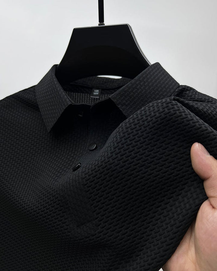 Black textured polo shirt on hanger, close-up of collar and buttons, hand touching fabric in studio.