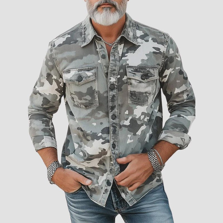 Man wearing gray camo shirt with rolled-up sleeves and button details against plain background.