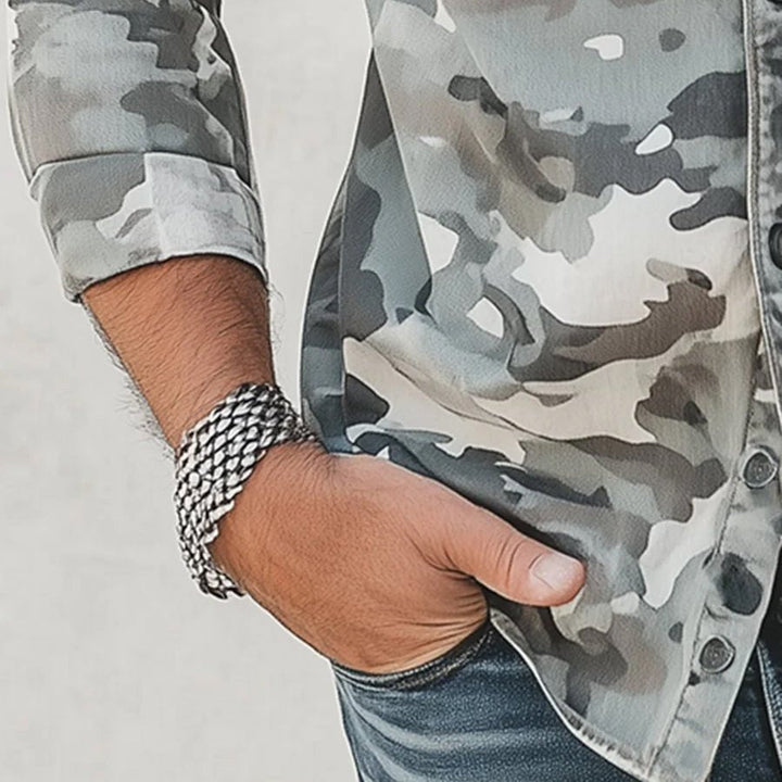 Close-up of gray camo shirt sleeve with bracelet and hand in pocket.