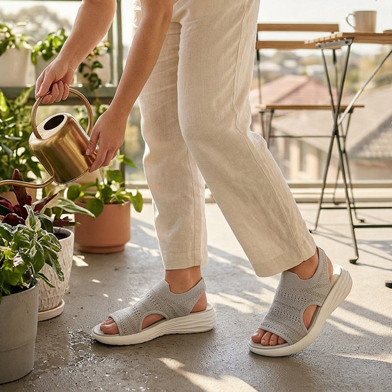 Gray knit platform sandals in a garden setting, person wearing light trousers and watering plants indoors on a balcony.