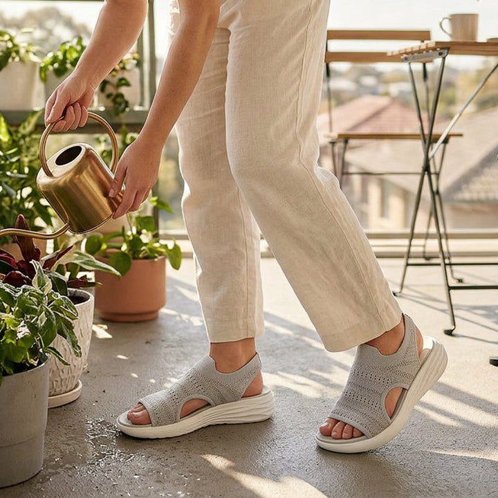 Gray knit platform sandals in a garden setting, person wearing light trousers and watering plants indoors on a balcony.
